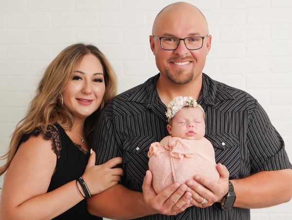 A happy couple proudly holding their newborn wrapped in a pink blanket with a floral headband.