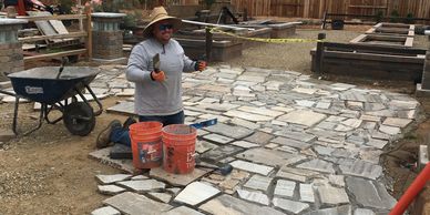 Man laying stone pathway in backyard garden under cloudy sky.