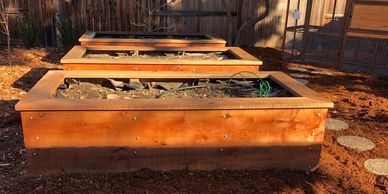 Three wooden raised garden beds in a backyard with mulch and a fenced area.