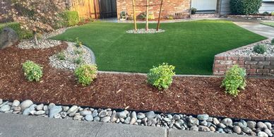 Well-maintained front yard with artificial grass, shrubs, and rock landscaping.