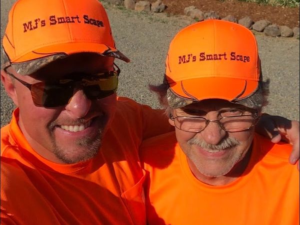 Two men wearing matching bright orange hats and shirts with "MJ's Smart Scape".