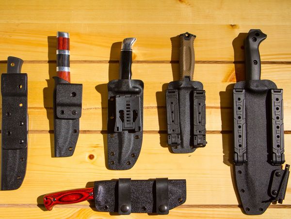 Five knives in black sheaths on a wooden surface.