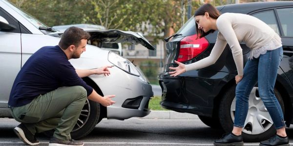 Two people arguing over a car accident in a parking lot.