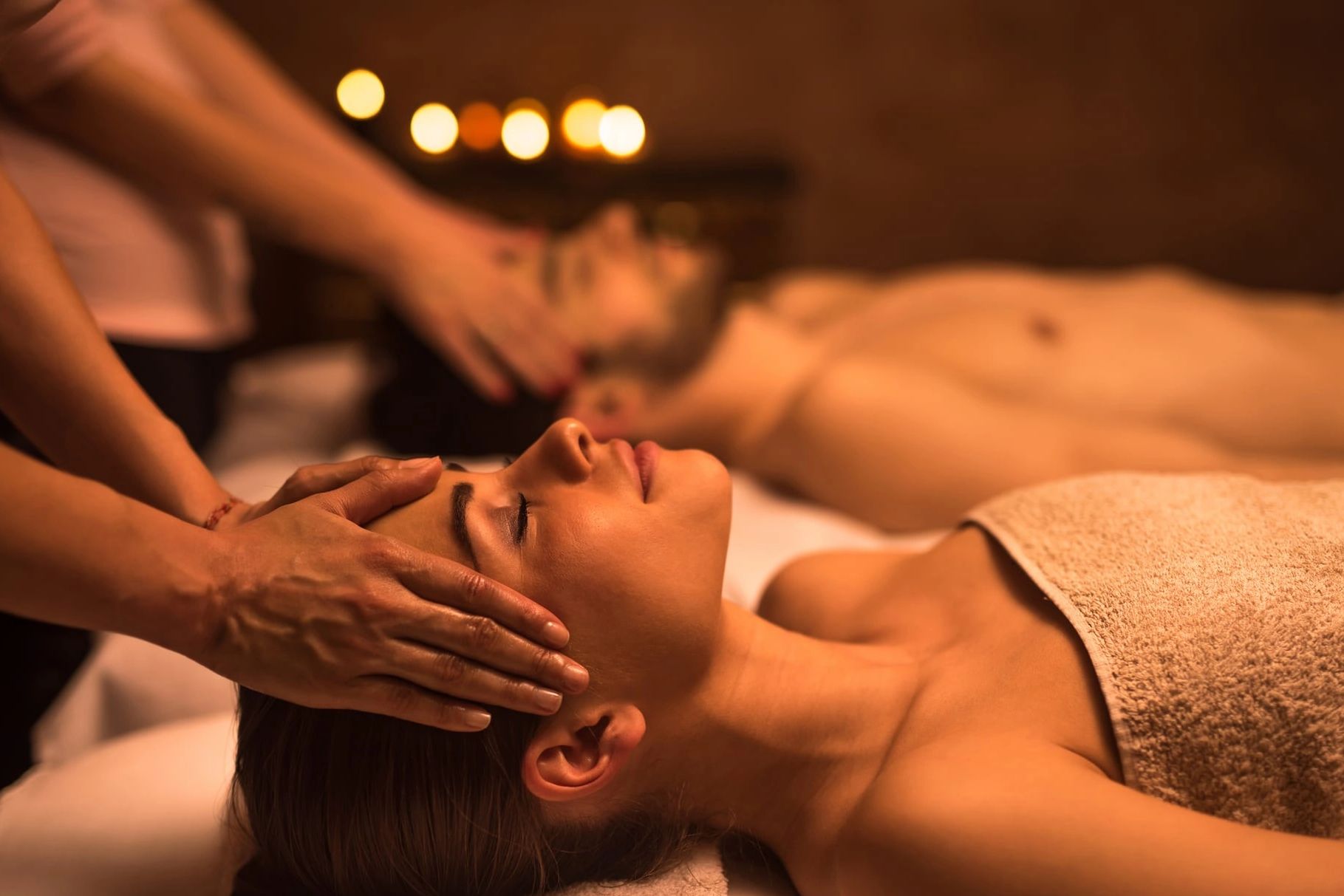 Two people enjoying a relaxing head massage in a dimly lit spa.