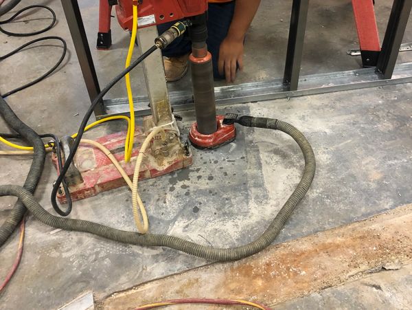 Worker operating a red core drilling machine on concrete floor.