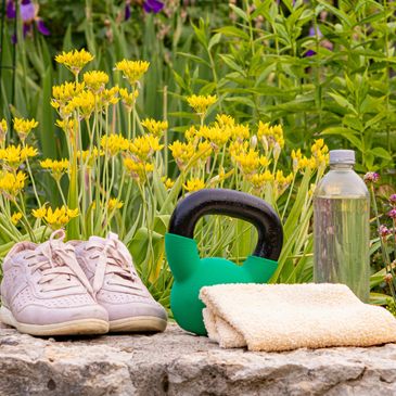 Workout essentials including shoes, kettlebell, towel, and water bottle outdoors.