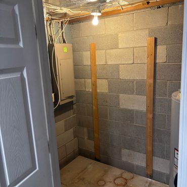 Empty basement corner with cinder block walls and wooden studs.
