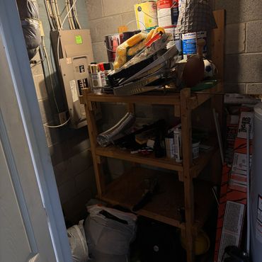 A cluttered wooden shelf in a dimly lit basement or storage area.