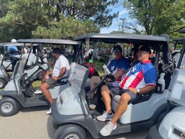 Two men in patriotic shirts sitting in a golf cart on a sunny day.