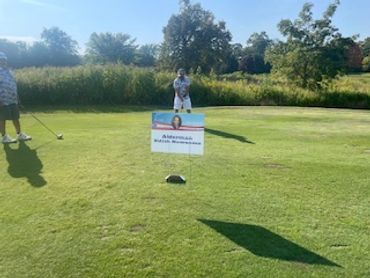 Two people playing golf on a sunny day with a sign on the green.