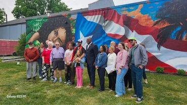 Group of people posing in front of a vibrant mural with a Puerto Rican flag.