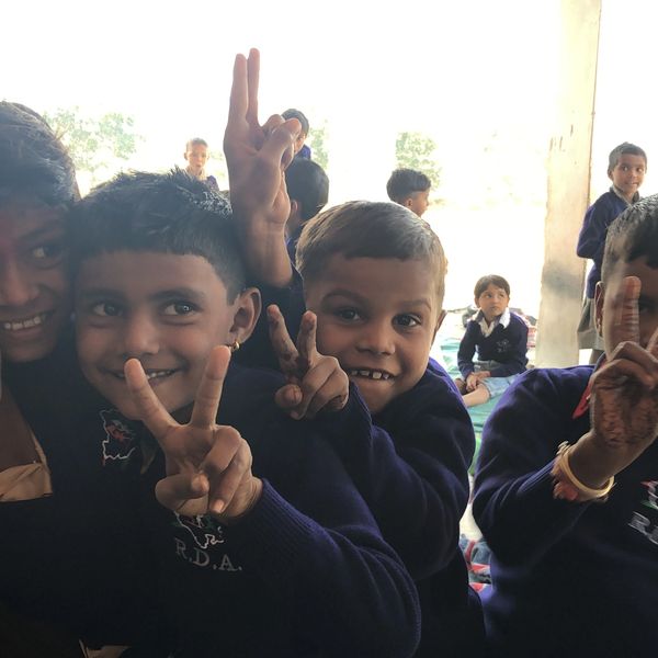 Group of smiling schoolboys showing peace signs indoors.