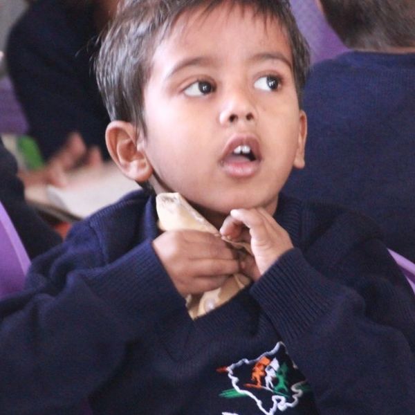 Young boy in a navy sweater sitting on a purple chair, looking thoughtfully.