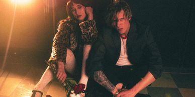 Two individuals sitting on the floor, one holding roses, with warm lighting.