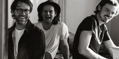Three men smiling and enjoying a candid moment together indoors.