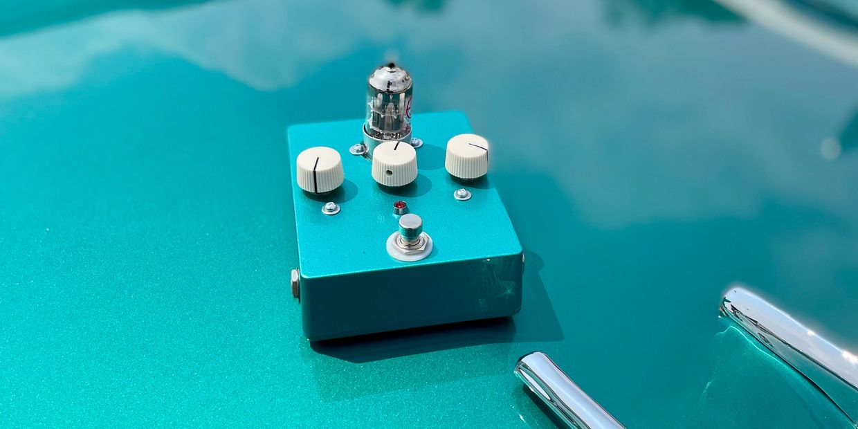 Turquoise guitar pedal with white knobs on a matching turquoise surface.