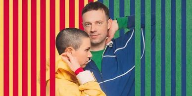 Two people posing against a colorful striped background, one in yellow and one in blue.