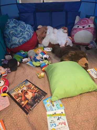 Cozy play area with stuffed animals, pillows, and children's books.