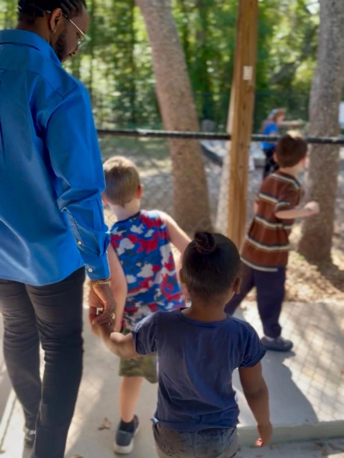 Adult holding a child's hand with kids playing outside.
