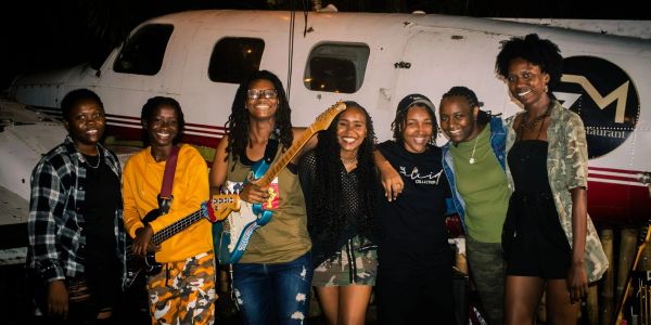 Group of seven friends posing in front of a small airplane.