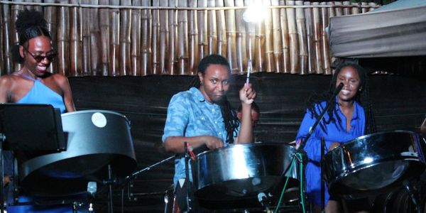 Three people playing steel drums on stage at night.