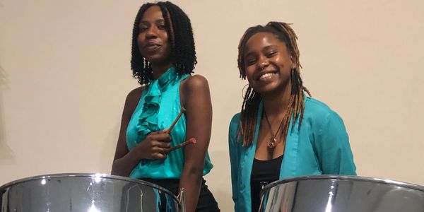 Two women playing steel drums and smiling.