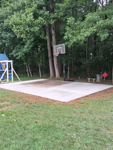 A concrete basketball court with a hoop and a playground nearby.