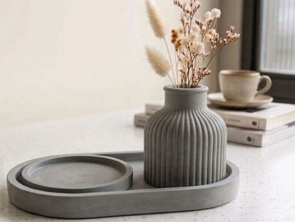 Minimalist grey vase with dried flowers on a matching tray, set on a white surface.
