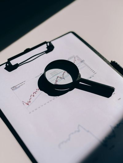 Magnifying glass highlights financial graph on clipboard for detailed analysis.