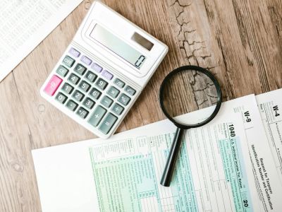 Calculator, magnifying glass, and tax forms on a wooden table.