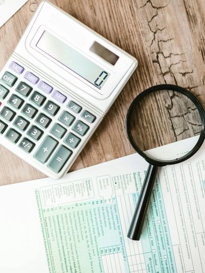 A calculator, magnifying glass, and tax form on a wooden table.