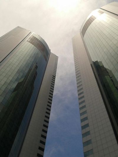Two modern skyscrapers stretch up towards a cloudy sky.