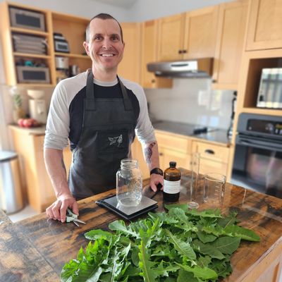 Man in apron smiling at kitchen counter with herbs and jars.