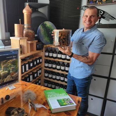 Man smiling and holding a container in a room filled with bottles and books.
