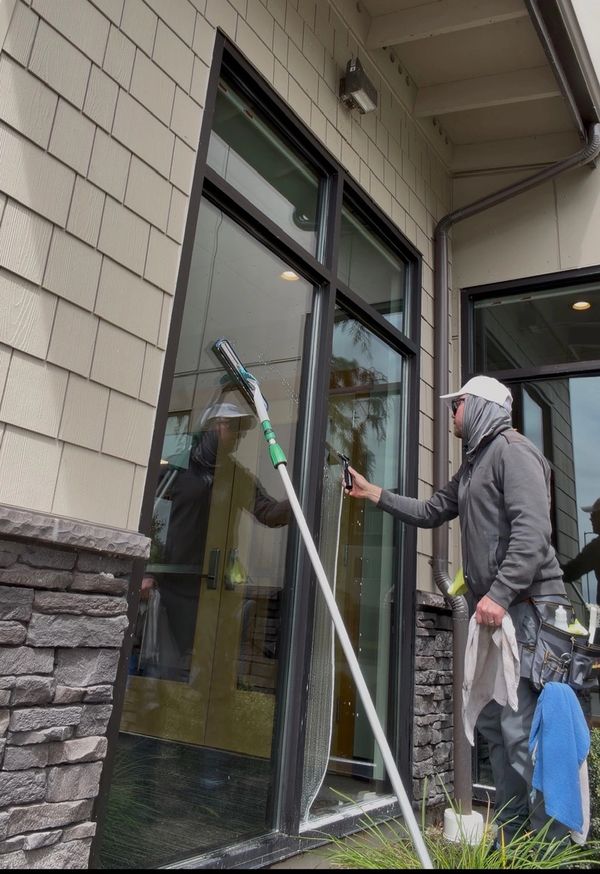 A man cleaning a large window with a squeegee and spray bottle.