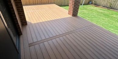 A backyard patio with wooden decking and a lawn enclosed by a wooden fence.