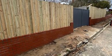New wooden fence with brick base along a roadside on a cloudy day.