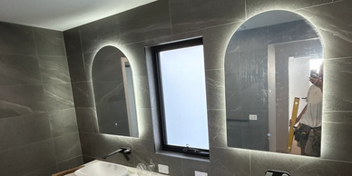 Modern bathroom with dual sinks and illuminated mirrors under construction.