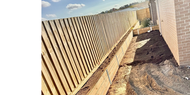 Newly constructed wooden retaining wall along a backyard fence on a sunny day.