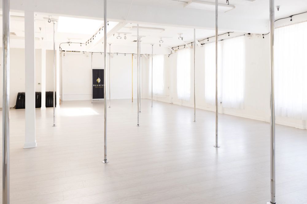 the empty pole studio floor, rows of poles, skylight and windows, BEEHIVE sign