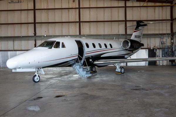Private jet parked inside a spacious hangar with open door and stairs.