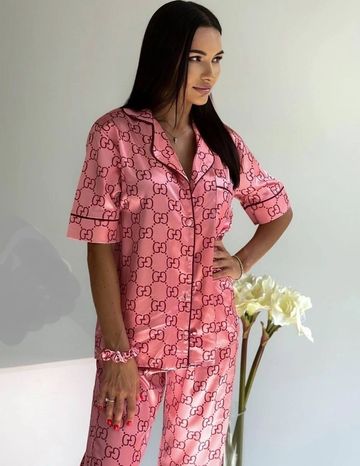 Woman in pink Gucci pajama set standing beside flowers.