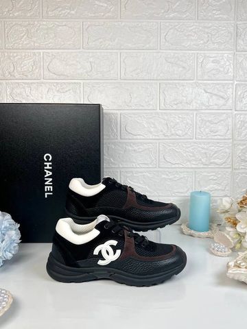 Black Chanel sneakers with white logo and box, set on a white surface with decorative flowers and candle.