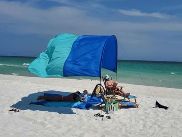Family relaxing under blue beach canopy on a sunny day.