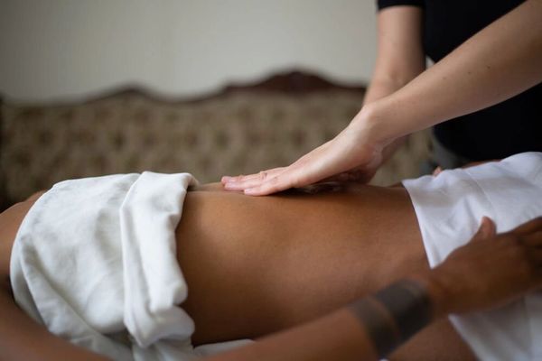 A person is lying down with and another person is performing Arvigo® massage 