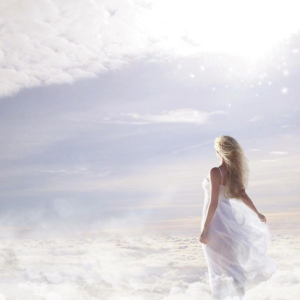 Woman in white dress stands amidst clouds under bright sky.