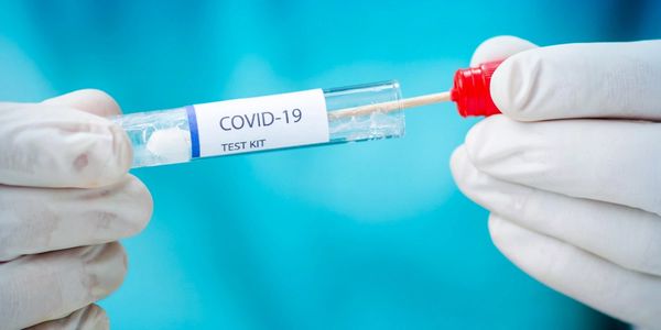 A COVID-19 test kit with a swab held by gloved hands.