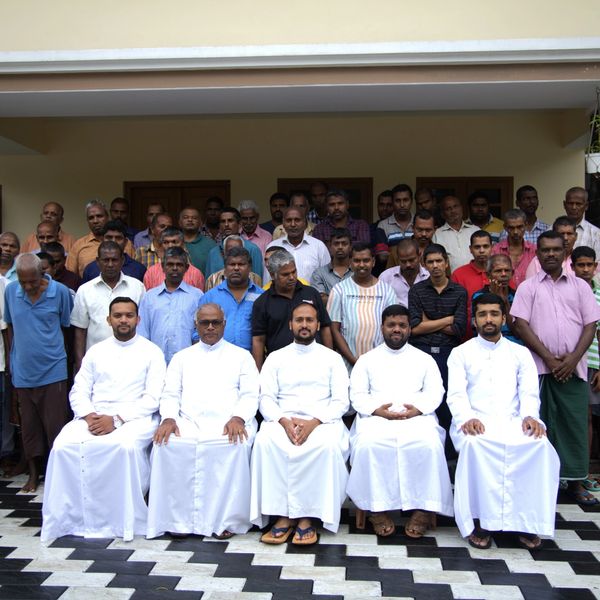 Group photo of men with five priests dressed in white seated in front.