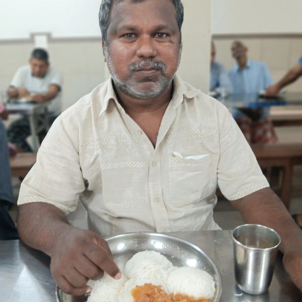 Man in beige shirt eating a meal with rice and boiled egg at a restaurant.