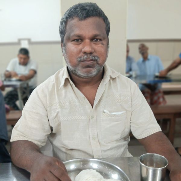 Man in beige shirt eating a meal with rice and boiled egg at a restaurant.